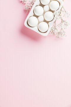 White eggs  in white ceramic holder and flowers on pink background