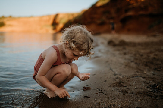 Small girl in swimsuit playing at beach, crouching, seraching for shells in the sand.