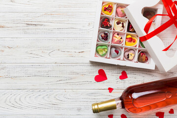 Bottle of red wine on colored background for Valentine Day with gift and chocolate. Heart shaped with gift box of chocolates top view with copy space
