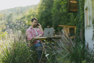 Man working in the garden on laptop, phone calling. Businessman working remotely from outdoor...