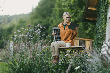 Woman in garden holding solar panel and tablet. Looking for solar panels grants, funds for...
