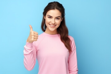 Happy young woman showing thumbs up over blue background.