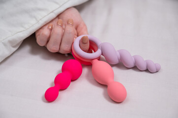 Woman holding three different anal beads while lying in bed. 