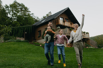 Family standing in front their house with solar panels on roof. Solar energy and sustainable lifestyle of young family. Concept of green energy and sustainable future for next generations.