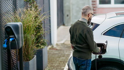 Businessman charging electric car before going to office. An electric vehicle charging station in...