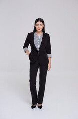 Full length portrait of an attractive smart asian businesswoman in suit standing with looking at camera isolated on gray background.