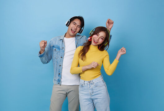 Smiling happy young Asian teen couple dancing enjoy playlist together romantic love isolated on blue studio background.