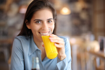 Happy woman drinking orange juice looking at camera