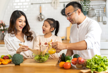 Portrait of enjoy happy love asian family father and mother with little asian girl daughter child having fun help cooking food healthy eat together with fresh vegetable salad ingredient in kitchen