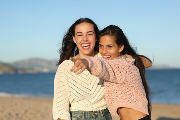 Two funny friends pointing away on the beach