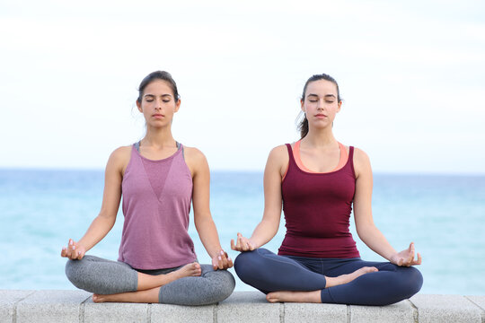 Two friends practicing yoga on the beach