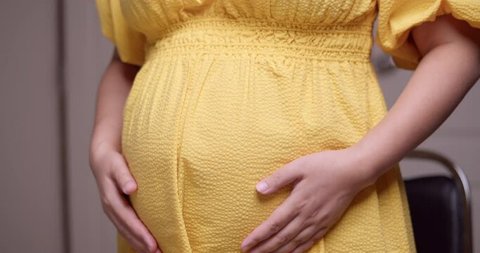 A pregnant woman caressing and stroking her own bulging baby bump with her hands in a circular motion.