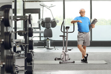 Mature man with an exercise mat standing next to a stationary bike at a gym