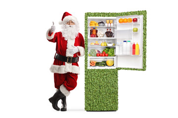 Santa claus leaning on a green eco friendly fridge and gesturing thumbs up