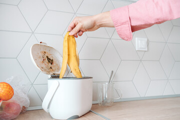 Man throwing banana peel into countertop composter. Concept of home composting, converting kitchen...