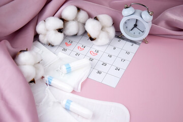Women's menstrual pads, tampons, female menstruation calendar and alarm clock on a pink background.