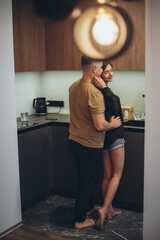 A young couple is standing in the kitchen. The guy sneaks up behind the girl and touches her waist...