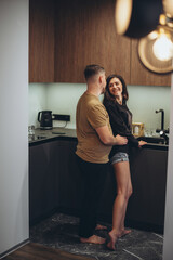 A young couple is standing in the kitchen. The guy sneaks up behind the girl and touches her waist...