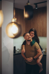 Guy and girl in the kitchen. A girl in shorts with bare feet jumped on the guy’s back, hugged him...