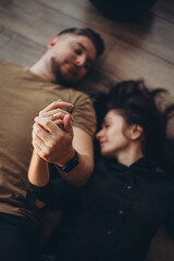 Girl and guy at home. The couple lies on the floor with their eyes closed and holds hands. Only the hands of the guy and the girl are in focus. Blurred background.