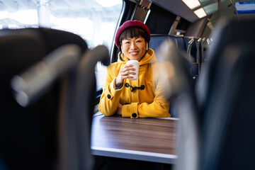 Smiling women listening to music and drinking coffee while commuting high speed train. - obrazy, fototapety, plakaty