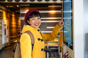 Woman in trendy coat ordering meal on self service interactive display inside fast food restaurant.
