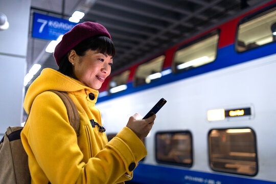 Woman at subway station platform checking train departure on smart phone.