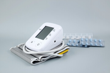 Digital blood pressure tonometer and pack of pills on a blue background with copy space.