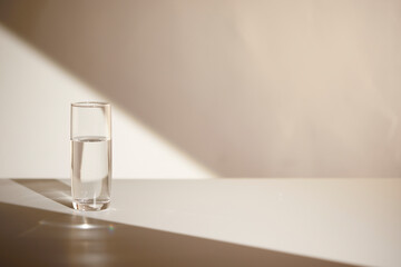 A water cup and shadow on a table in the sunlight.