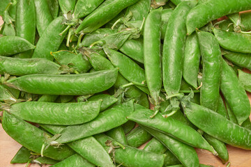 green ripe plucked pea pods on a wooden kitchen cutting board close-up. flat lay