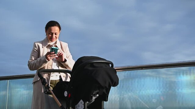 Smiling happy woman mother taking photo on smartphone of her child sleeping in baby pram, while walking together on the coastline