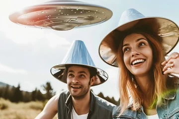 Poster man and woman holding metallic hats, exaggerated emotions, futuristic spaceship, ufos in the sky, conspiracy theory concept © zgurski1980