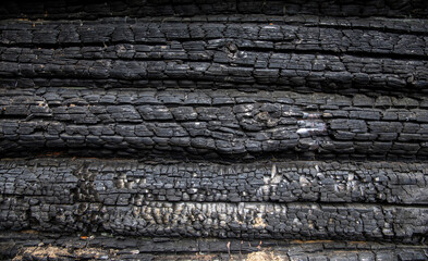 Charred wooden logs of a barn, bathhouse, house after a fire.