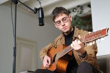 Young man musician singing song playing classical guitar at music studio. Male wearing earphones to...