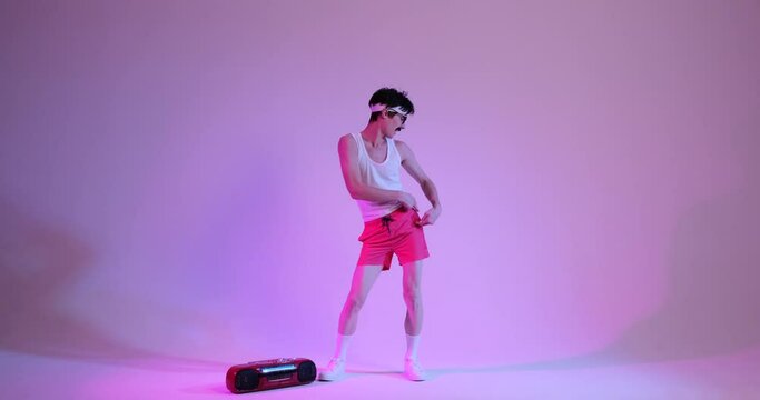 Happy, amusing 80s young Caucasian man with mustache, listening music, dancing with cassette player over purple background in neon light.