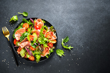 Salad in black bowl at dark background.