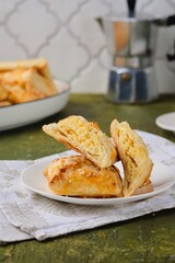 Unsweetened pastries, puff pastry envelopes with cheese filling on a white plate on a green concrete background.
