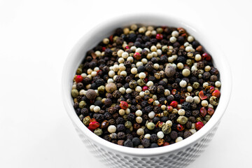 A mixture of pepper varieties with peas on the white plate on the white background. Heap of various pepper. Mix of red, black and white peppercorn seeds isolated on white. Top view