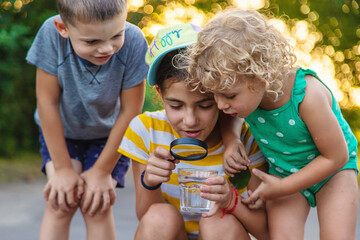 Children look with a magnifying glass into a glass of water. Selective focus.