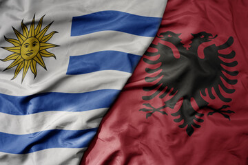 big waving national colorful flag of albania and national flag of uruguay .