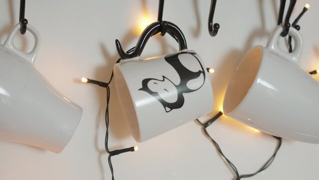 Image of white coffee mugs with cow spots hanging on a metal rack intertwined with warm fairy lights