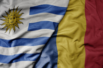 big waving national colorful flag of romania and national flag of uruguay .