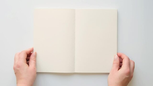 Female hands open a book with blank pages, top view. 4K video on white background