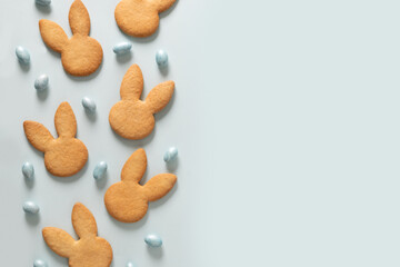 Easter homemade cookies shaped of bunny and blue chocolate sweets candy eggs on pastel blue background. View from above. Festive food and snacks. Greeting card with copy space