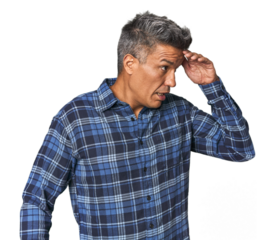 Middle-aged Latino man looking far away keeping hand on forehead.