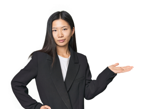 Young Chinese woman in business suit showing a copy space on a palm and holding another hand on waist.
