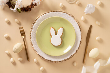 Easter table setting with white and green plate, bunny cookies, eggs on beige background. View from...