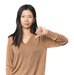 Young Chinese woman in studio setting showing thumb down, disappointment concept.