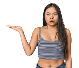 Young Chinese woman in gray top, studio impressed holding copy space on palm.