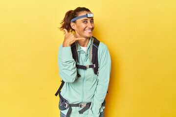 Mountain gear and frontal light on yellow showing a mobile phone call gesture with fingers.